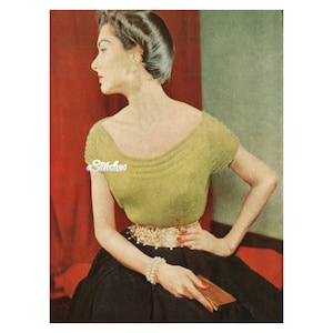 Può includere: Una donna indossa una maglia di lana verde con scollo rotondo e maniche corte. Indossa una gonna nera e una collana di perle. Tiene una piccola pochette.