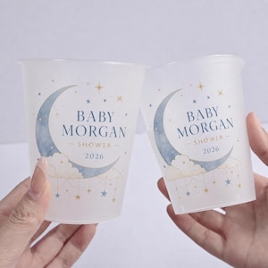 May include: Two translucent plastic cups featuring a blue watercolor crescent moon, fluffy clouds, and small gold and blue stars. The text reads BABY MORGAN SHOWER 2026 in blue and gold lettering. The design includes hanging star accents.
