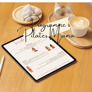 Peut inclure: Une tablette numérique affichant un programme de Pilates, avec le texte "Programme Pilates Mama". L'image comprend une tasse de café, un verre d'eau et une assiette de friandises blanches, le tout sur une table en bois. Un stylet blanc est également présent.