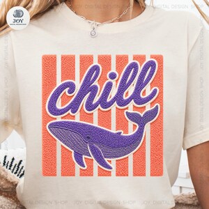 Puede incluir: Camiseta color crema con una ilustración de ballena morada y la palabra "chill". El diseño incluye un fondo a rayas naranja y blanco texturizado, creando un ambiente relajado y juguetón.