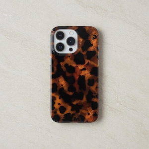 May include: A phone case featuring a tortoiseshell design. The case has a glossy finish with brown, black, and amber hues. The camera lenses are visible at the top.