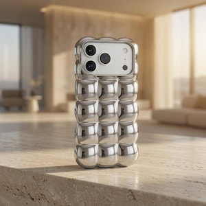 May include: A silver iPhone case with a unique, textured design. The case features a series of rounded, square-shaped bumps across its surface. The phone's camera lenses are visible at the top. The case is made of a shiny, reflective material.