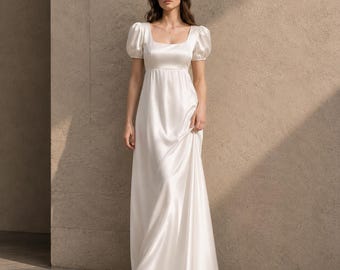 May include: A floor-length ivory satin gown featuring a square neckline, short puff sleeves, and an empire waistline. The dress has a smooth, lustrous finish and a flowing skirt that extends to the floor, creating a clean and simple silhouette.