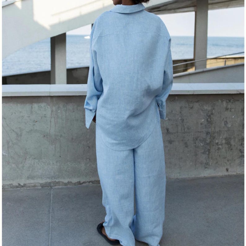 May include: A light blue long-sleeved button-down shirt and matching wide-leg trousers. The set is crafted from a textured fabric with a visible weave. The shirt features a classic collar and long sleeves with cuffs, while the trousers have a loose fit.