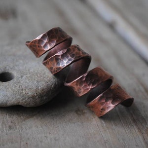 Puede incluir: Un anillo de cobre en espiral con textura martillada. El anillo está hecho de múltiples bandas de cobre que están retorcidas juntas.