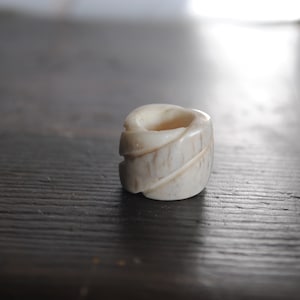 May include: A white bone bead with a spiral design. The bead is smooth and polished.