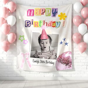 May include: A rectangular fabric backdrop featuring the text Happy Birthday in colorful cutout-style letters. A central black and white photo shows a child wearing a pink glitter party hat. Below the photo, the text reads Emily's 36th Birthday.