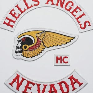 May include: Set of embroidered patches featuring the words "HELLS ANGELS" in red on a white arched background, a winged skull emblem, the letters "MC", and the word "NEVADA" in red on a white arched background.