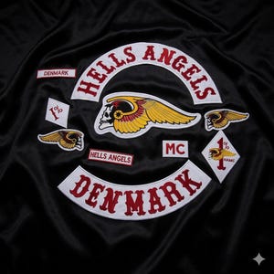 May include: A black fabric garment featuring embroidered Hells Angels patches. The design includes a large winged skull emblem, the text Hells Angels, Denmark, MC, and 1% symbols in red, white, and yellow thread on a dark, smooth, satin-like material.