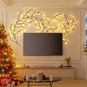 May include: A decorated Christmas tree with red and gold ornaments stands next to a wall with a large flat-screen TV. Above the TV, decorative branches with warm white lights are arranged. A coffee table holds popcorn and drinks.