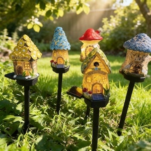 Op de afbeelding: Een verzameling op zonne-energie werkende tuinverlichting in de vorm van grillige fee&euml;nhuizen en paddenstoelen. De huizen hebben gele, blauwe en bruine daken, sommige met het woord "Welcome". Ze staan in een grasveld, verlicht door de zon.