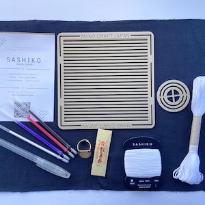 Può includere: Un kit iniziale per ricamo Sashiko composto da un quadrato di tessuto blu scuro, una dima a griglia quadrata in legno con etichetta MANO CRAFT JAPAN, una guida circolare in legno, filo bianco, un ditale, quattro pennarelli e una guida.