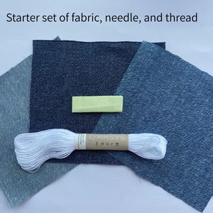 May include: A starter set of fabric, needle, and thread featuring three square pieces of denim fabric in varying shades of blue, a small yellow needle case, and a skein of white embroidery thread with a label reading Sashiko.
