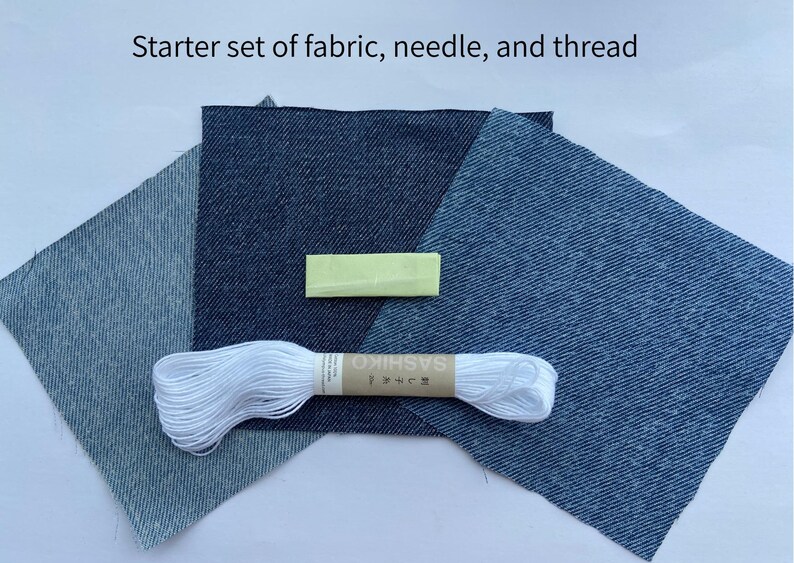 May include: A starter set of fabric, needle, and thread featuring three square pieces of denim fabric in varying shades of blue, a small yellow needle case, and a skein of white embroidery thread with a label reading Sashiko.