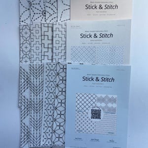 Może przedstawiać: Kolekcja rozpuszczalnych w wodzie arkuszy do haftowania z napisem Stick & Stitch. Arkusze zawierają r&oacute;żne czarne geometryczne wzory nadrukowane na białej tkaninie. Każdy arkusz zawiera instrukcje odklejania, przyklejania, haftowania i rozpuszczania. Niekt&oacute;re arkusze zawierają kod QR.
