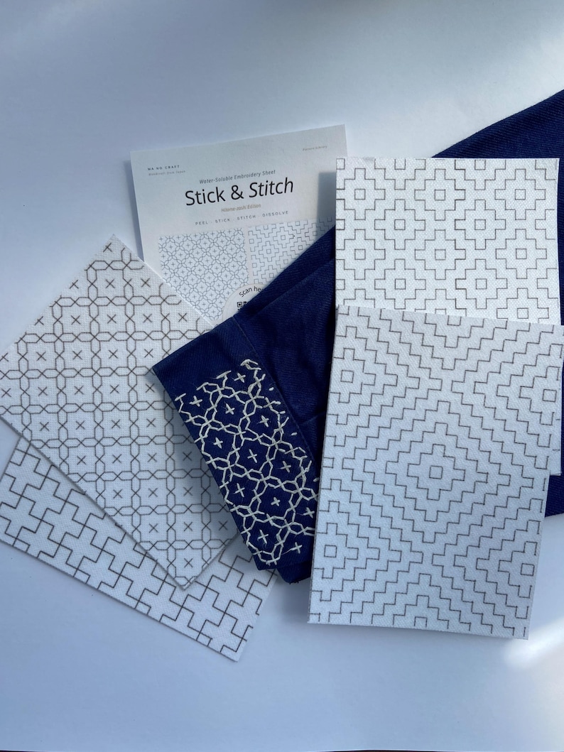 Może przedstawiać: Rozpuszczalne w wodzie arkusze do haftowania z napisem Stick & Stitch z r&oacute;żnymi geometrycznymi wzorami w czarnym tuszu na białym papierze. Ciemnoniebieski kawałek materiału ma biały haftowany wz&oacute;r w kratkę, dołączono arkusz instrukcji.