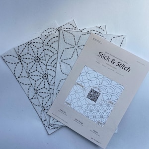 May include: A set of white water-soluble embroidery sheets labelled Stick & Stitch. The sheets feature black geometric patterns including star and fan designs. The top sheet includes a QR code, instructions to peel, stick, stitch, and dissolve.