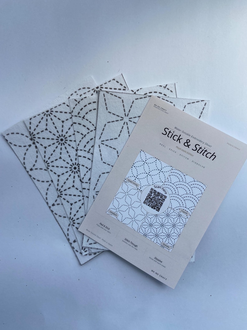 May include: A set of white water-soluble embroidery sheets labelled Stick & Stitch. The sheets feature black geometric patterns including star and fan designs. The top sheet includes a QR code, instructions to peel, stick, stitch, and dissolve.