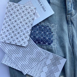 May include: Close-up of denim fabric with visible stitching and patches. Several white cards with geometric patterns are placed on the denim. One card has the text "Stick & Stitch". The patterns include diamond and zigzag designs.