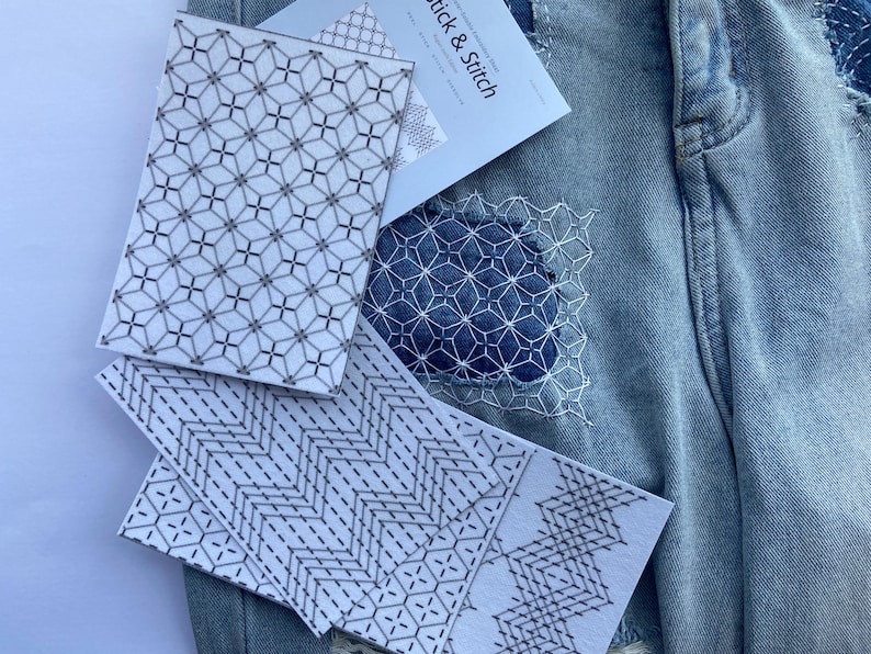 May include: Close-up of denim fabric with visible stitching and patches. Several white cards with geometric patterns are placed on the denim. One card has the text "Stick & Stitch". The patterns include diamond and zigzag designs.