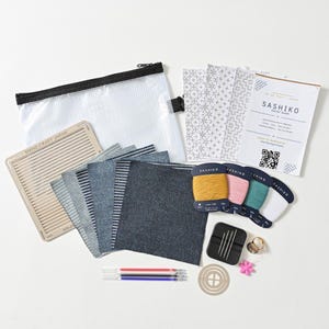 Puede incluir: Un kit de inicio de bordado Sashiko que incluye una bolsa transparente con cremallera, una plantilla de madera, cuadrados de tela azul, cuatro carretes de hilo en amarillo, rosa, verde y blanco, agujas, un dedal, un alfiler de flor y una guía con código QR.