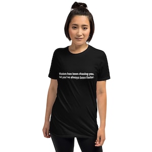 Puede incluir: Camiseta negra con el texto blanco: "La sabiduría te ha estado persiguiendo, pero siempre has sido más rápido". La camiseta es de manga corta y cuello redondo.