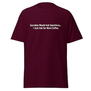 Puede incluir: Camiseta granate con texto blanco: "Socrates Would Ask Questions... I Just Ask for More Coffee." La camiseta es de manga corta y cuello redondo.