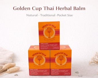 Puede incluir: Tres cajas naranjas de Golden Cup Thai Herbal Balm están apiladas. Cada caja tiene una franja roja y un emblema dorado. El texto "Golden Cup Balm" es visible en cada caja, junto con las palabras "Natural, Traditional, Pocket Size."