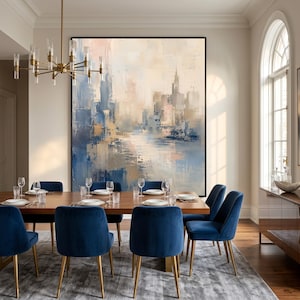 May include: A large rectangular abstract painting featuring a city skyline in shades of blue, beige, and soft pink. The artwork is displayed on a wall above a long wooden dining table surrounded by six blue velvet chairs with gold metal legs.