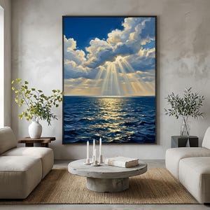 May include: Large framed artwork depicting a seascape with a blue ocean under a bright blue sky filled with fluffy white clouds. Golden sunlight streams through the clouds, illuminating the water. The painting is displayed in a modern living room.