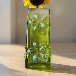 Pode incluir: Um vaso quadrado de vidro verde-limão com padrões de flores em relevo na superfície. O vaso tem um acabamento translúcido e contém um girassol amarelo com um centro castanho escuro que se estende a partir da abertura superior.