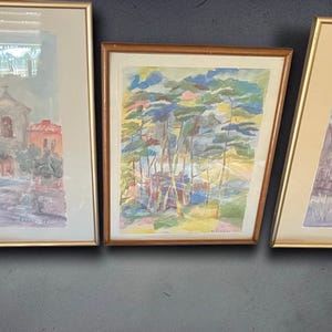Könnte beinhalten: Drei gerahmte Aquarellbilder, die nebeneinander angeordnet sind. Das linke Bild zeigt einen Stadtplatz mit Gebäuden, das mittlere zeigt eine Waldszene mit buntem Laub und das rechte zeigt eine Landschaft mit kahlen Bäumen und Gebäuden.