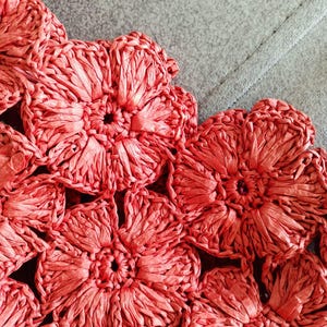 Peut inclure: Gros plan sur un motif floral tissé de couleur corail. Les fleurs sont faites d'une matière texturée, peut-être du raphia ou une fibre similaire, et sont disposées en motif répétitif. Le motif semble faire partie d'une pièce plus grande, comme un sac ou un accessoire.