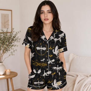 May include: Black pajama set with a dragon and moon pattern. The short-sleeved top and shorts have white trim and a button-up front. The design includes the text "Wing Leader" and "Thorn Wing".