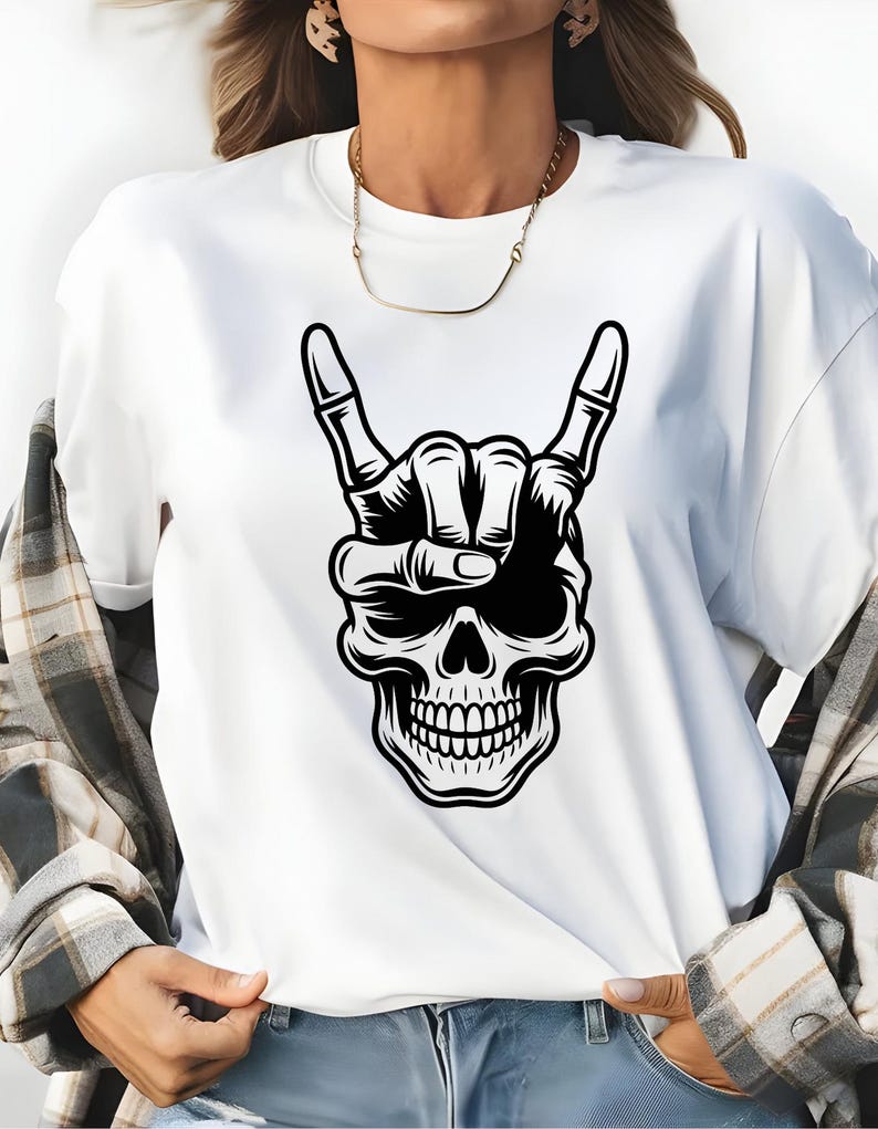 May include: A white short-sleeved t-shirt featuring a black graphic print of a human skull with a skeletal hand making a rock and roll hand gesture above its head. The shirt is worn with a grey and white plaid button-down shirt and blue jeans.