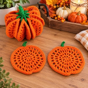 May include: A three-dimensional crocheted orange pumpkin with a green stem and two flat, circular crocheted orange pumpkin coasters, each featuring a green stem and an openwork lattice pattern, arranged on a wooden surface.