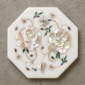 Op de afbeelding: Witte achthoekige decoratieve marmeren plaat met ingelegd bloemmotief. Twee grote rozen van parelmoer zijn omgeven door groene, blauwe en bruine accenten. Het stuk heeft een gepolijste afwerking.