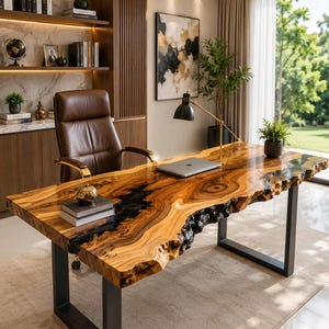May include: A live edge wood desk with a natural grain pattern and a black resin inlay, supported by two black metal U-shaped legs. The desk surface holds a silver laptop, a small potted plant, and a stack of books with a gold apple-shaped object.