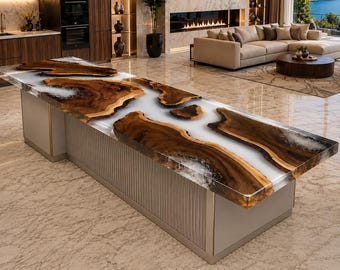May include: A large kitchen island featuring a live edge wood slab tabletop with a translucent white resin river inlay. The base is constructed from light grey vertical panels with gold trim accents, providing a structured support for the wood surface.