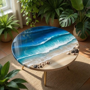 Può includere: Tavolino rotondo con design oceano in resina. Il tavolo presenta una finitura lucida con una rappresentazione di onde oceaniche in tonalità di blu e bianco, che conducono a una spiaggia sabbiosa. È sostenuto da tre gambe in legno. Diametro di circa 90 cm.