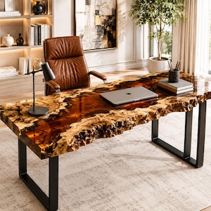 Peut inclure: Un bureau rectangulaire composé d'un plateau en bois à bord brut avec une incrustation en résine ambrée brillante, soutenu par deux pieds en métal noir en forme de U. Le bureau porte un ordinateur portable argenté, une lampe et des livres.