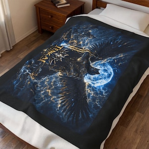 May include: A black blanket featuring a detailed illustration of a large bird with outstretched wings, a full moon, and the word "TENKAI" in gold lettering. The design uses shades of blue, gold, and black, creating a celestial theme.