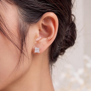 Peut inclure: Une boucle d'oreille à clou en or ornée d'une pierre précieuse transparente de taille rectangulaire, maintenue par quatre griffes. La boucle d'oreille est placée sur le lobe, mettant en valeur une monture en or poli fixant la pierre à facettes.