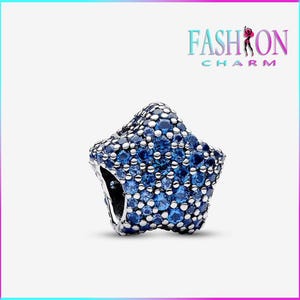Puede incluir: Un charm en forma de estrella con base plateada, incrustado con piedras preciosas azules y blancas. El charm tiene un diseño tridimensional y está sobre un fondo blanco. El texto "FASHION CHARM" es visible en la esquina superior derecha.