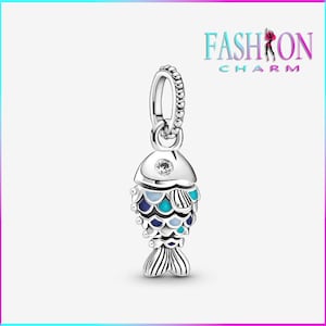 May include: A silver fish charm with blue, teal, and white enamel scales. The charm has a small clear gem on its head and a textured loop for attaching to a bracelet or necklace. The word "FASHION CHARM" is in the upper right corner.