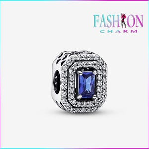 May include: A silver charm with a rectangular, deep blue gemstone at the center, surrounded by a double halo of small, clear gemstones. The charm has a decorative, openwork design on the sides. The text "FASHION CHARM" is in the upper right corner.