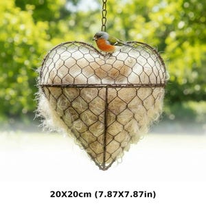 May include: Heart-shaped hanging planter made of wire mesh, filled with natural fibers. A small bird with orange, green, and gray feathers perches on top. The planter measures 7.87 x 7.87 inches.