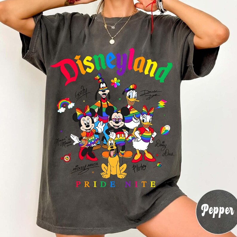 Puede incluir: Camiseta gris oscuro con la palabra "Disneyland" en colores arco&iacute;ris y personajes de dibujos animados como Mickey Mouse y Donald Duck. El texto "Pride Nite" est&aacute; en la parte inferior.