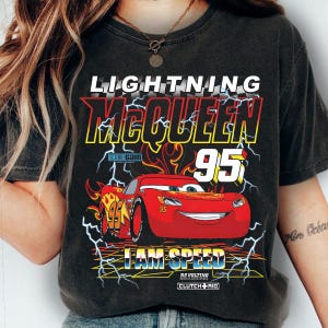 Op de afbeelding: Donkergrijze t-shirt met Lightning McQueen uit de film Cars. Het ontwerp bevat de tekst "LIGHTNING McQUEEN 95" en "I AM SPEED" met een rode raceauto en bliksemaccenten.