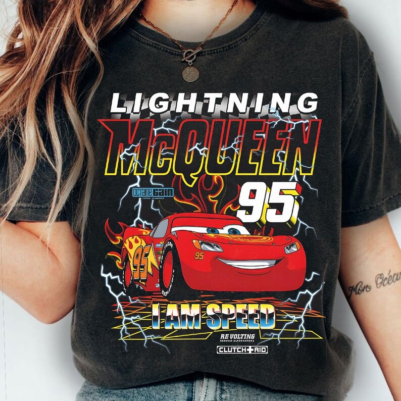 Op de afbeelding: Donkergrijze t-shirt met Lightning McQueen uit de film Cars. Het ontwerp bevat de tekst "LIGHTNING McQUEEN 95" en "I AM SPEED" met een rode raceauto en bliksemaccenten.